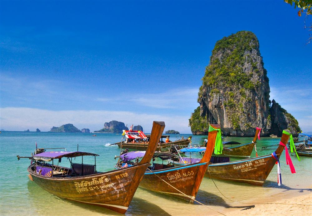 Traditional longtail boats on a beach beneath a limestone cliff