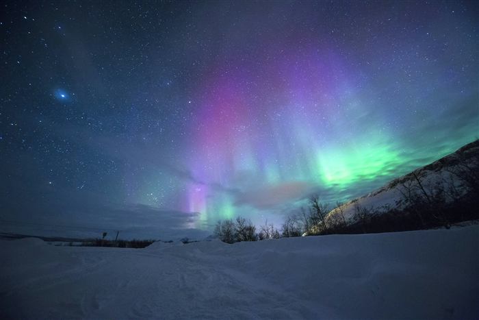 Green and violet aurora over a snowy mountain