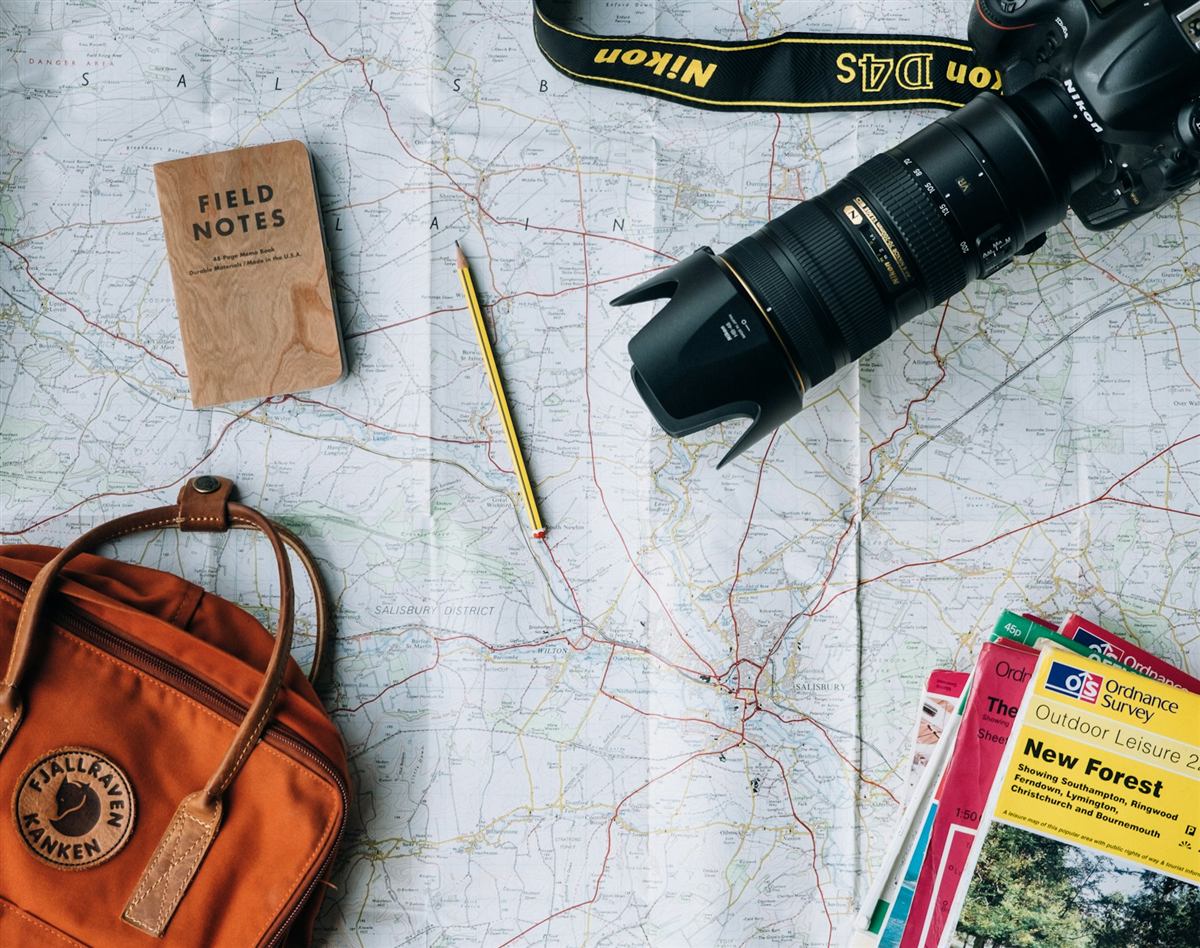 Travel planning desk with a paper map, camera, backpack and notebook