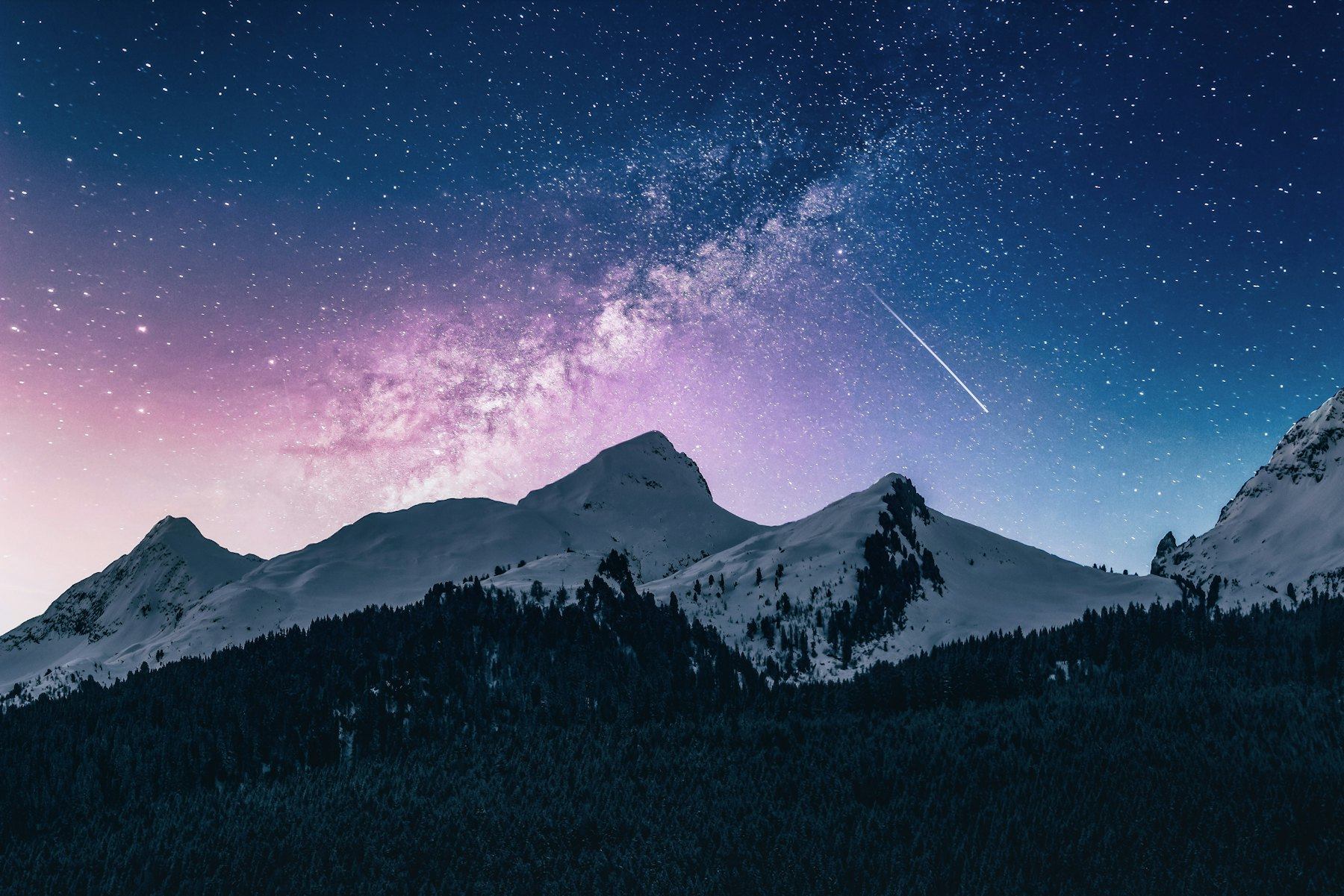 Milky Way glowing above snow-covered mountain peaks at night