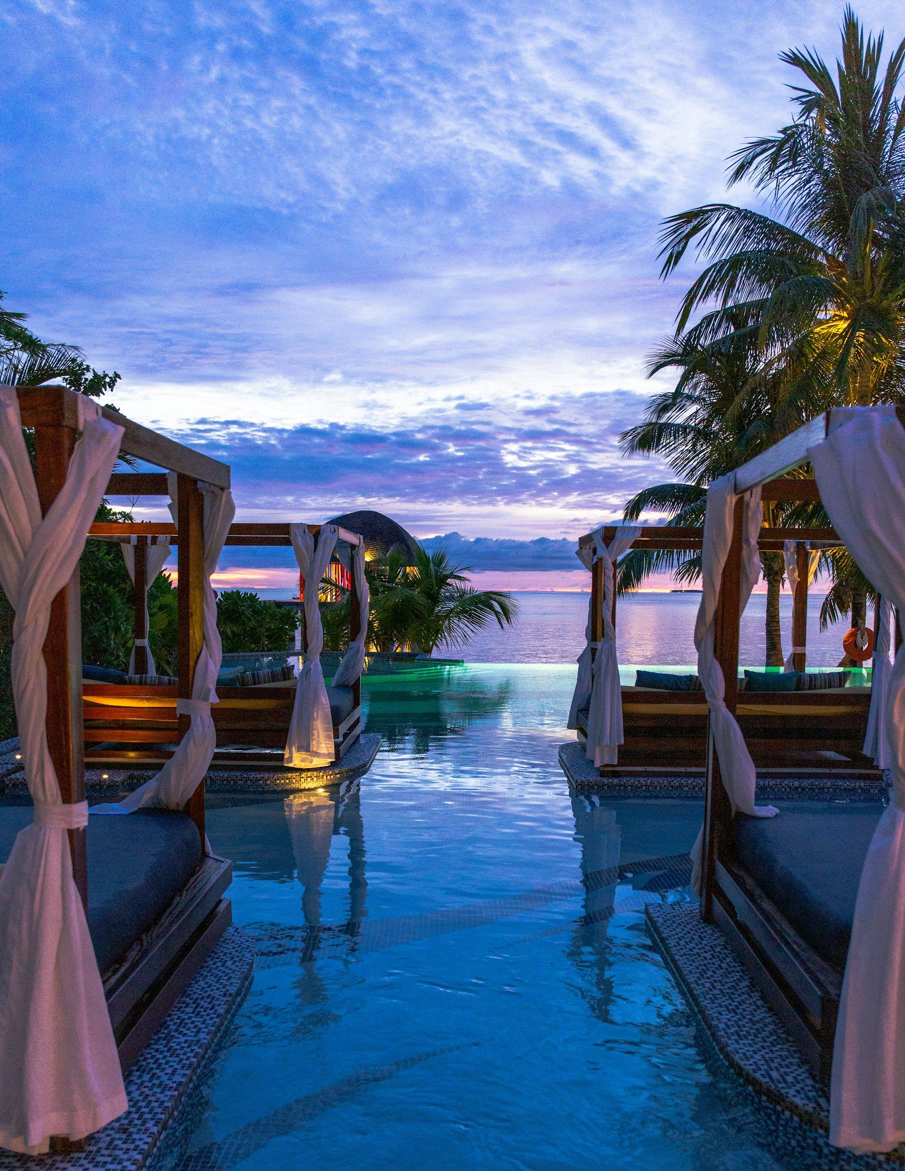 Resort cabanas beside a glowing pool at dusk